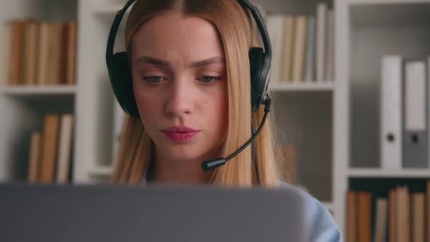 Közelíts rá a fehér női irodai dolgozóra a headset konferencia videón, aki laptoppal telefonál. Komoly nő üzletasszony ügyfélszolgálat menedzser beszél webkamera távolság távoli chat - Felvétel, videó