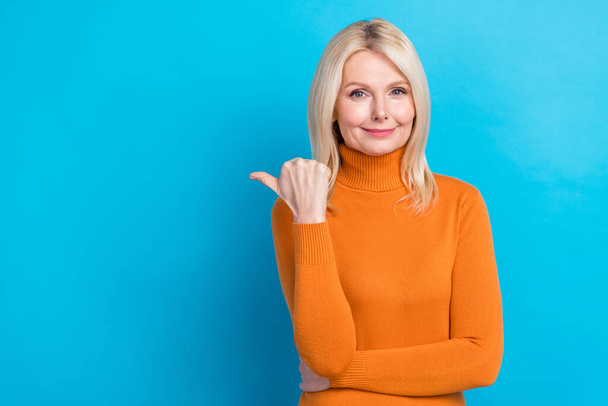 Zdjęcie blond włosy emerytowany wiek firma pani nosić modne pomarańczowy sweter punkt palec puste miejsce reklama izolowane na tle koloru cyjan. - Zdjęcie, obraz