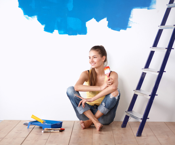 πορτρέτο του ζωγράφου γυναίκα που κάθεται στο πάτωμα κοντά τοίχο μετά από την ζωγραφική. - Φωτογραφία, εικόνα
