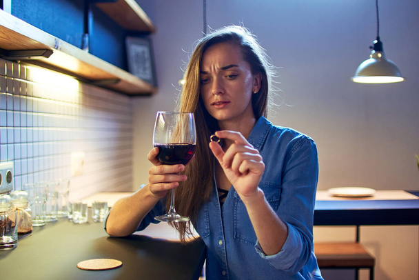 Lonely depressed unhappy upset pensive woman with marriage ring and red wine glass sitting alone during going through relationship breakup and divorce  - Foto, Bild