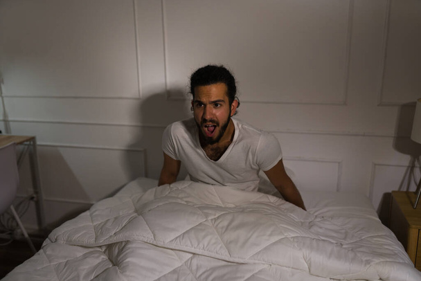 Scared hispanic man screaming feeling afraid after waking up from a scary nightmare in the middle of the night - Photo, Image