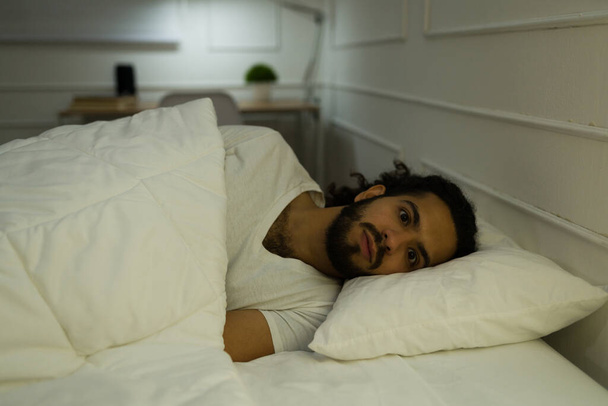 Ahdistunut nuori mies, jolla on unihäiriö ja joka kärsii unettomuudesta yrittäessään nukkua myöhään yöllä makuuhuoneessaan - Valokuva, kuva