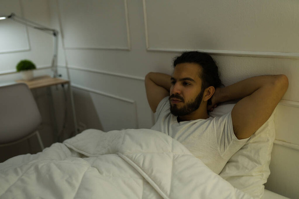 Handsome man in his 20s with his arms behind the head thinking about his problems and having sleeping problems - Фото, зображення