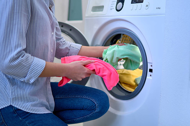 Woman loads washing machine with colored clothes at laundry day - Фото, изображение