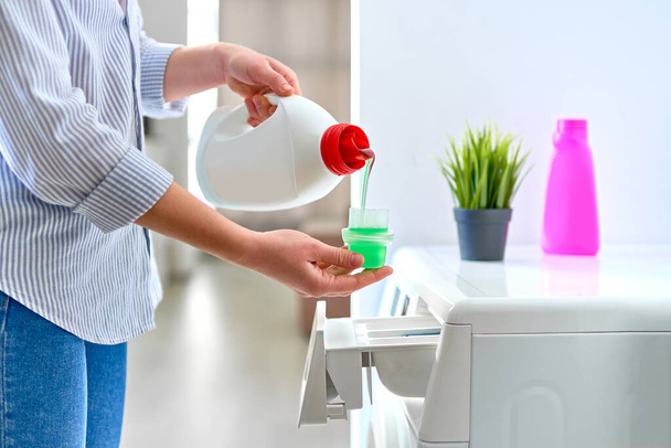 Woman housewife using fabric softener detergent gel for washing machine at laundry day  - Valokuva, kuva