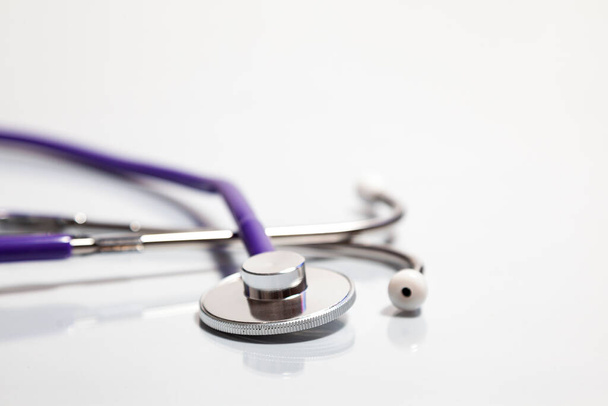 Close-up of a stethoscope's bell over a white surface where is reflected. The tubing is purple and earpieces are white. - 写真・画像