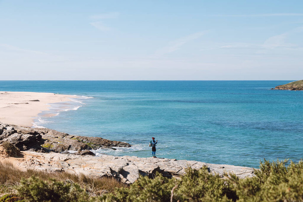 Muž ve sportovním oblečení a s batohem fotí pobřeží Atlantiku poblíž Porto Covo v Portugalsku. Zachycování momentů na mobilním telefonu. - Fotografie, Obrázek