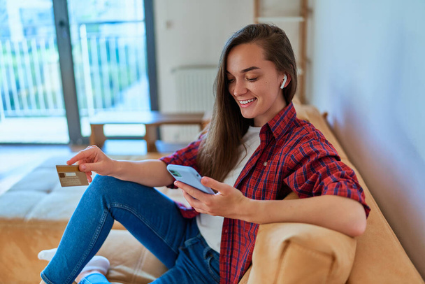 Beautiful casual happy modern young girl using smartphone and credit card for shopping online, paying and ordering goods via the Internet - Φωτογραφία, εικόνα