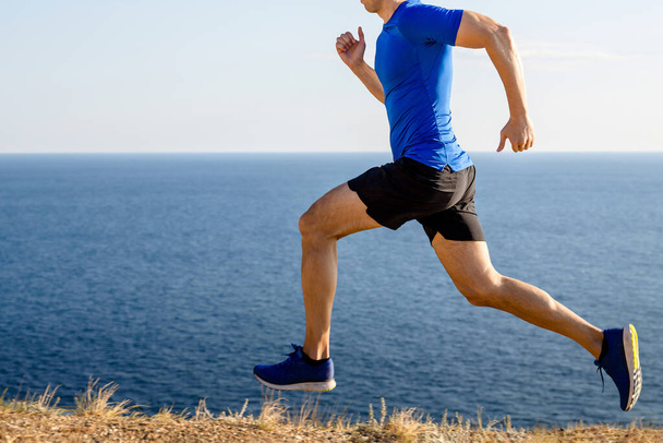 mężczyzna biegnie górski szlak w tle morza i nieba, latem jogging wzdłuż wybrzeża - Zdjęcie, obraz