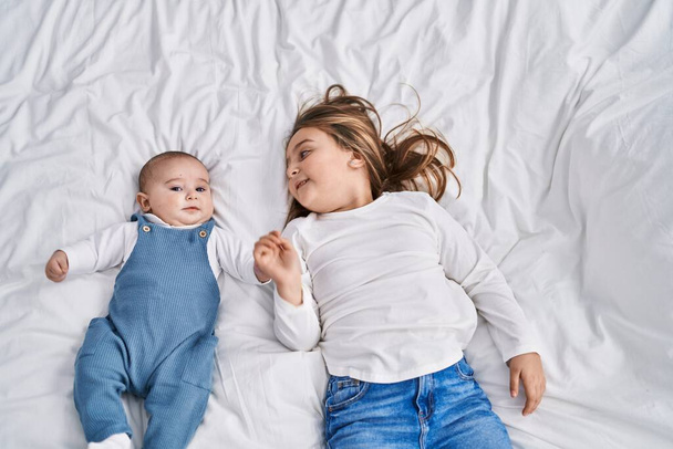 Hermano y hermana sonriendo confiados acostados juntos en la cama en el dormitorio - Foto, Imagen