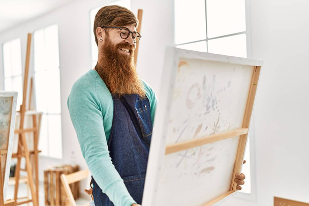 Young redhead man smiling confident holding canvas draw at art studio - Photo, Image