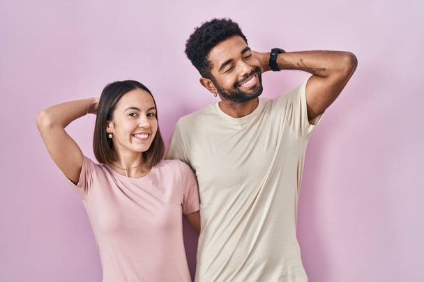Young hispanic couple together over pink background smiling confident touching hair with hand up gesture, posing attractive and fashionable  - Fotografie, Obrázek