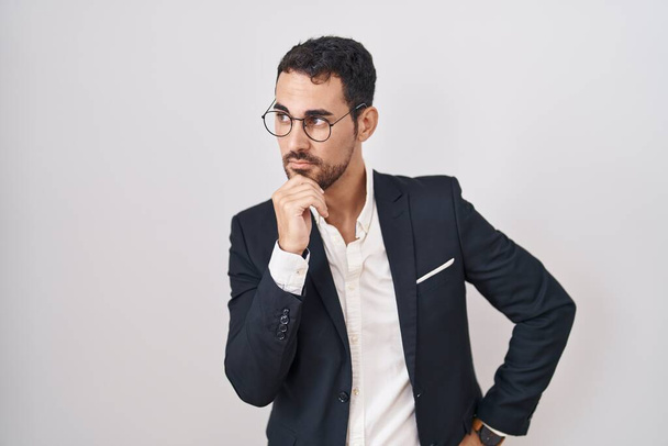Handsome business hispanic man standing over white background with hand on chin thinking about question, pensive expression. smiling with thoughtful face. doubt concept.  - Φωτογραφία, εικόνα