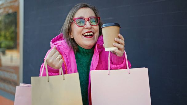 Mulher hispânica madura com cabelos grisalhos sorrindo indo às compras bebendo café na rua - Foto, Imagem