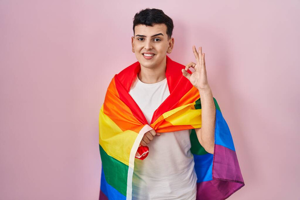 Non binary person holding rainbow lgbtq flag doing ok sign with fingers, smiling friendly gesturing excellent symbol  - Photo, Image