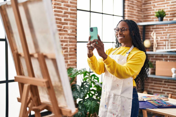 アフリカ系アメリカ人の女性アーティストは、アートスタジオで描くためにスマートフォンで写真を撮る - 写真・画像