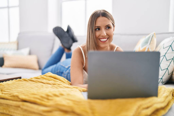 Young beautiful hispanic woman using laptop lying on table at home - Photo, Image