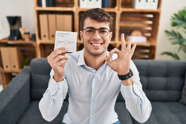 Молодий іспаномовний чоловік тримає приховану картку запису, роблячи знак з пальцями, усміхнений дружній жест відмінний символ
  - Фото, зображення