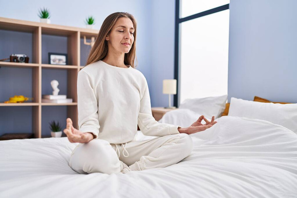 Young woman doing yoga exercise sitting on bed at bedroom - Фото, зображення