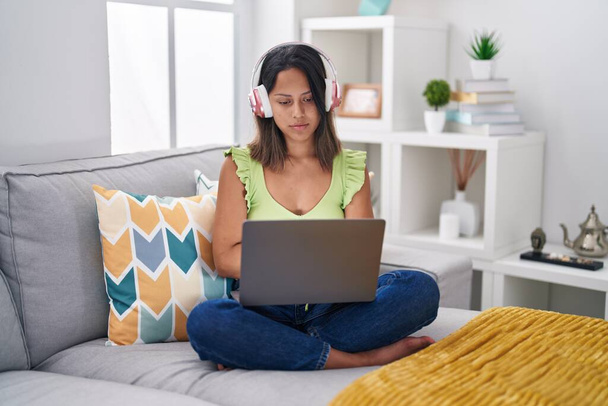 Jeune femme hispanique utilisant un ordinateur portable à la maison détendue avec une expression sérieuse sur le visage. simple et naturel regardant la caméra.  - Photo, image
