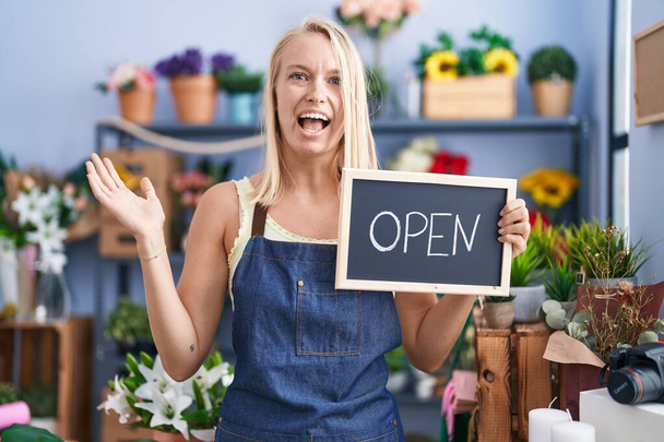 Young caucasian woman working at florist with open sign celebrating victory with happy smile and winner expression with raised hands  - Photo, Image