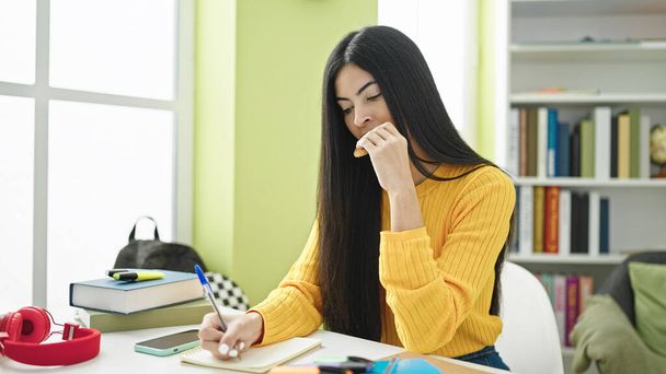 Fiatal gyönyörű spanyol nő diák írás jegyzetek eszik cookie-t könyvtár egyetem - Fotó, kép