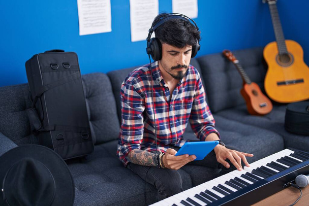 Young hispanic man musician playing piano keyboard using touchpad at music studio - Fotó, kép