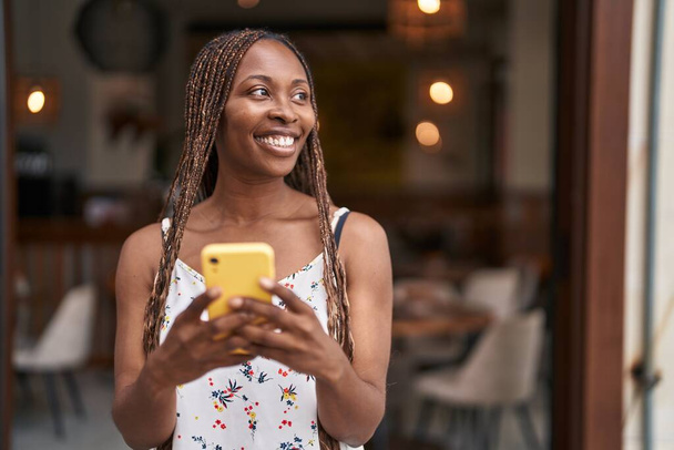 Afrikai amerikai nő mosolygós magabiztos segítségével smartphone kávézó terasz - Fotó, kép