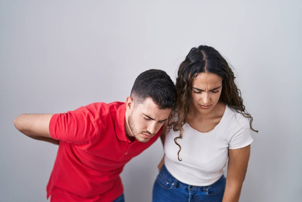 Jovem casal hispânico em pé sobre fundo isolado sofrendo de dor nas costas, tocando de volta com a mão, dor muscular  - Foto, Imagem