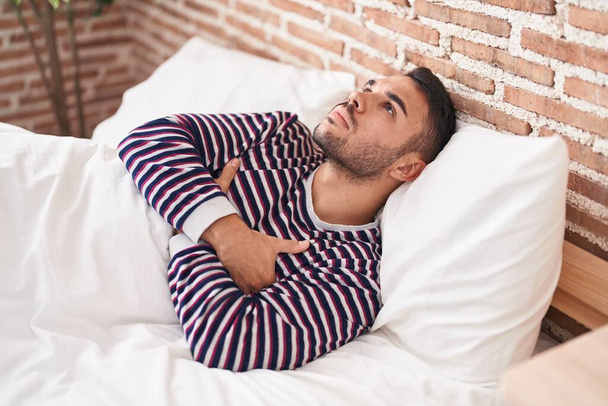 Young hispanic man stressed lying on bed at bedroom - Photo, Image