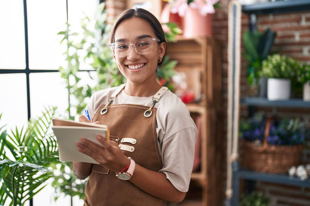 Young beautiful hispanic woman florist smiling confident writing on notebook at florist - Photo, Image