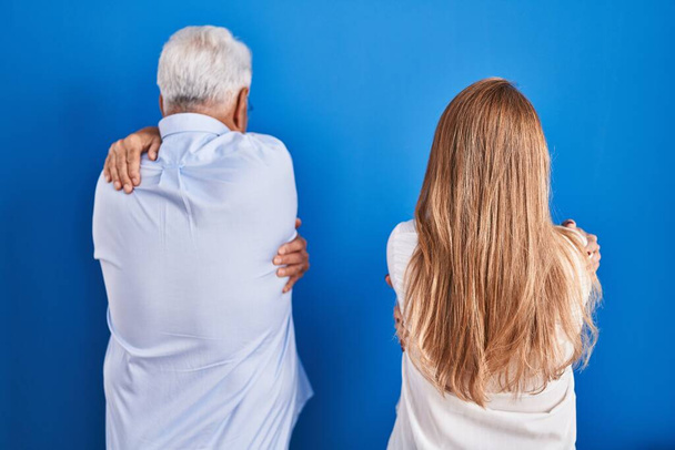 Orta yaşlı İspanyol bir çift mavi arka planda dikilip mutlu ve pozitif bir şekilde sarılıyor. Sevgi ve özgüven.  - Fotoğraf, Görsel