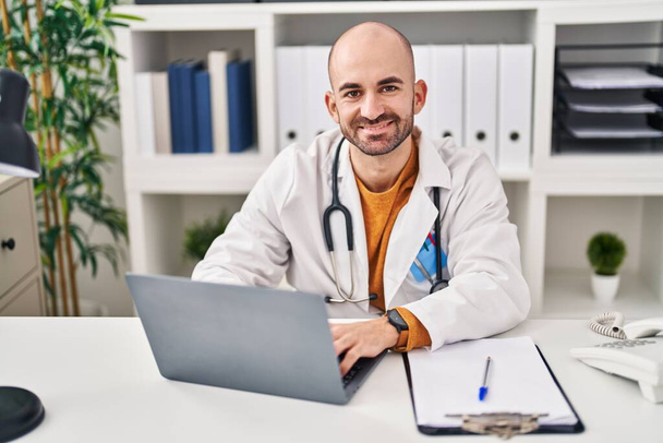 Junger Mann in Arztuniform mit Laptop in Klinik - Foto, Bild