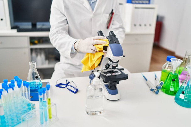 Fiatal spanyol férfi tudós takarítás mikroszkóp a laboratóriumban - Fotó, kép