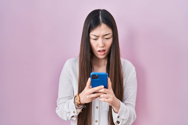 Čínská mladá žena pomocí smartphone psaní zprávu v šoku tvář, vypadá skeptický a sarkastický, překvapen s otevřenými ústy  - Fotografie, Obrázek