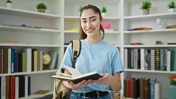 Nuori kaunis latino nainen opiskelija lukeminen kirja seisoo kirjaston yliopistossa - Valokuva, kuva