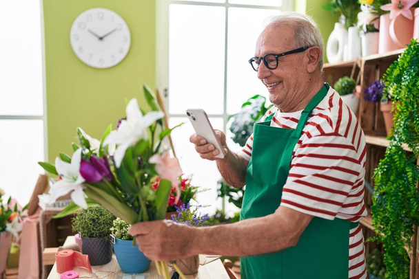 Floristería hombre de pelo gris de mediana edad hacer foto a las flores por teléfono inteligente en la tienda de flores - Foto, Imagen