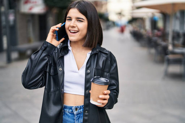 Young beautiful hispanic woman talking on the smartphone drinking coffee at street - Foto, imagen