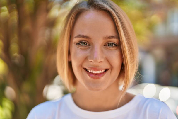 Young blonde woman smiling confident standing at park - 写真・画像