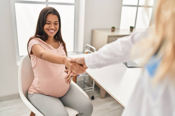 Young latin woman pregnant and doctor shake hands at clinic - Foto, Bild