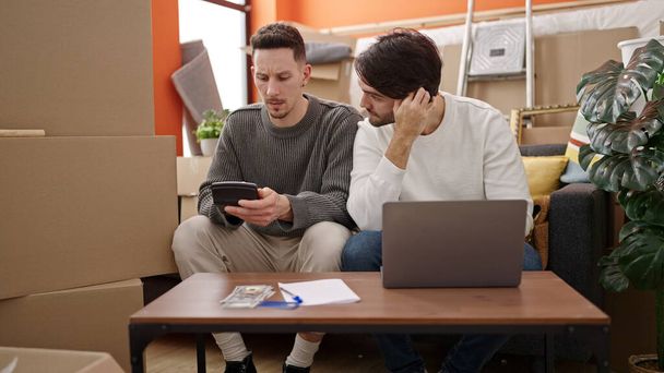 Двое мужчин используют ноутбук, считая доллары в новом доме - Фото, изображение