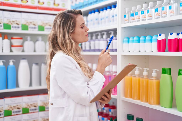 Young blonde woman pharmacist writing on document at pharmacy - Foto, Imagen