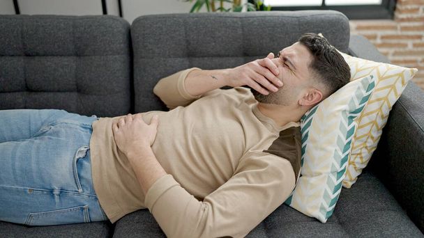 młody arabski człowiek cierpiący na ból brzucha leżący na kanapie w domu - Zdjęcie, obraz