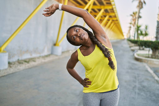 Αφροαμερικανή γυναίκα που φοράει αθλητικά που τεντώνει το χέρι της στο δρόμο - Φωτογραφία, εικόνα