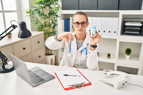 Young doctor woman wearing uniform and stethoscope with angry face, negative sign showing dislike with thumbs down, rejection concept  - Foto, immagini