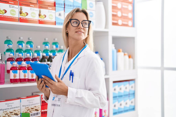 Young blonde woman pharmacist using touchpad working at pharmacy - Foto, immagini