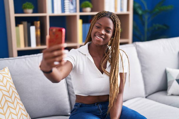 Afroamerykanka zrobić selfie przez smartfona siedzi na kanapie w domu - Zdjęcie, obraz