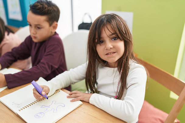 Мальчики и девочки сидят за столом и рисуют на блокноте в классе - Фото, изображение
