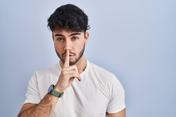 Hispanic man with beard standing over white background asking to be quiet with finger on lips. silence and secret concept.  - Photo, Image