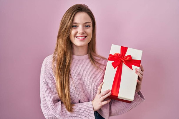 Młoda biała kobieta trzymająca prezent uśmiechnięta ze szczęśliwym i chłodnym uśmiechem na twarzy. wykazujące zęby.  - Zdjęcie, obraz
